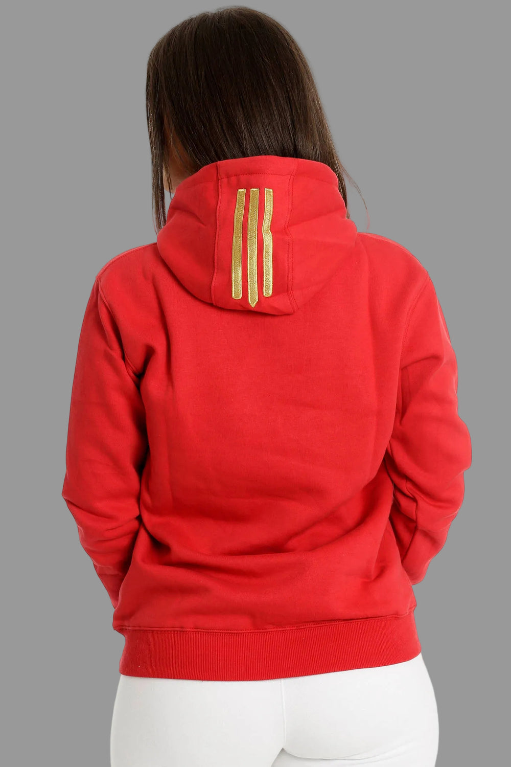 Dos du hoodie rouge avec trois rayures dorées sur la capuche. Le mannequin porte un pantalon blanc.
