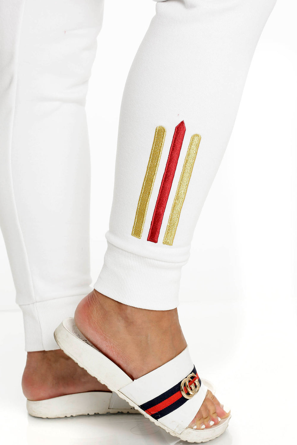 À la cheville du pantalon blanc, deux rayures dorées et une rouge, au-dessus d'un bord-côte.