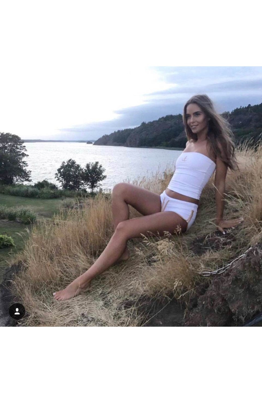 Lumière du soir au bord de l'eau. Le modèle est assise dans les hautes herbes en bandeau blanc et short blanc.