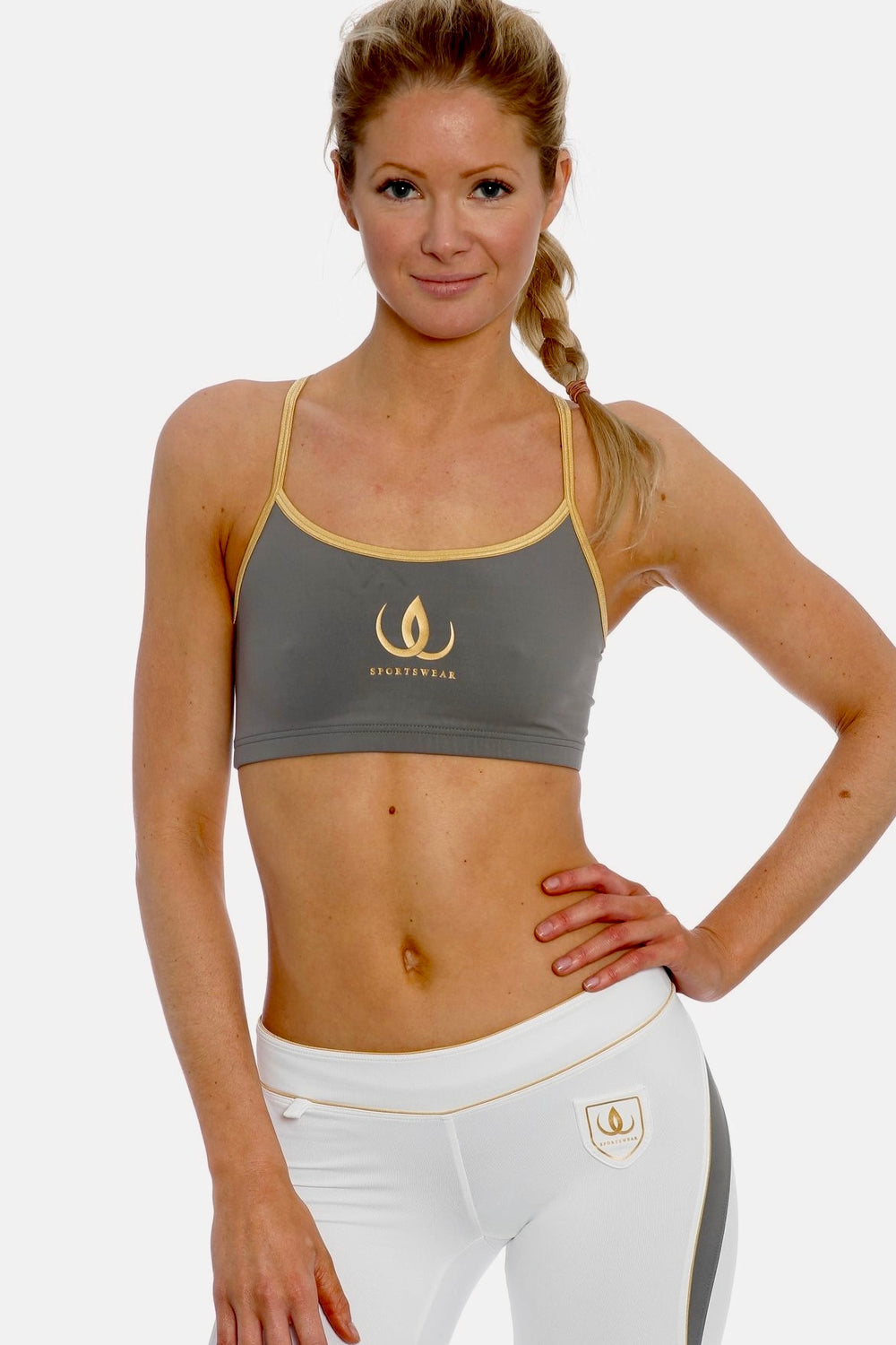 Haut de sport gris à bretelles dorées et logo doré, porté avec un legging blanc à panneau gris.