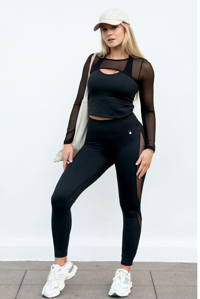 Un haut noir à manches en mesh, une casquette et un tote bag blanc sont portés avec le legging.