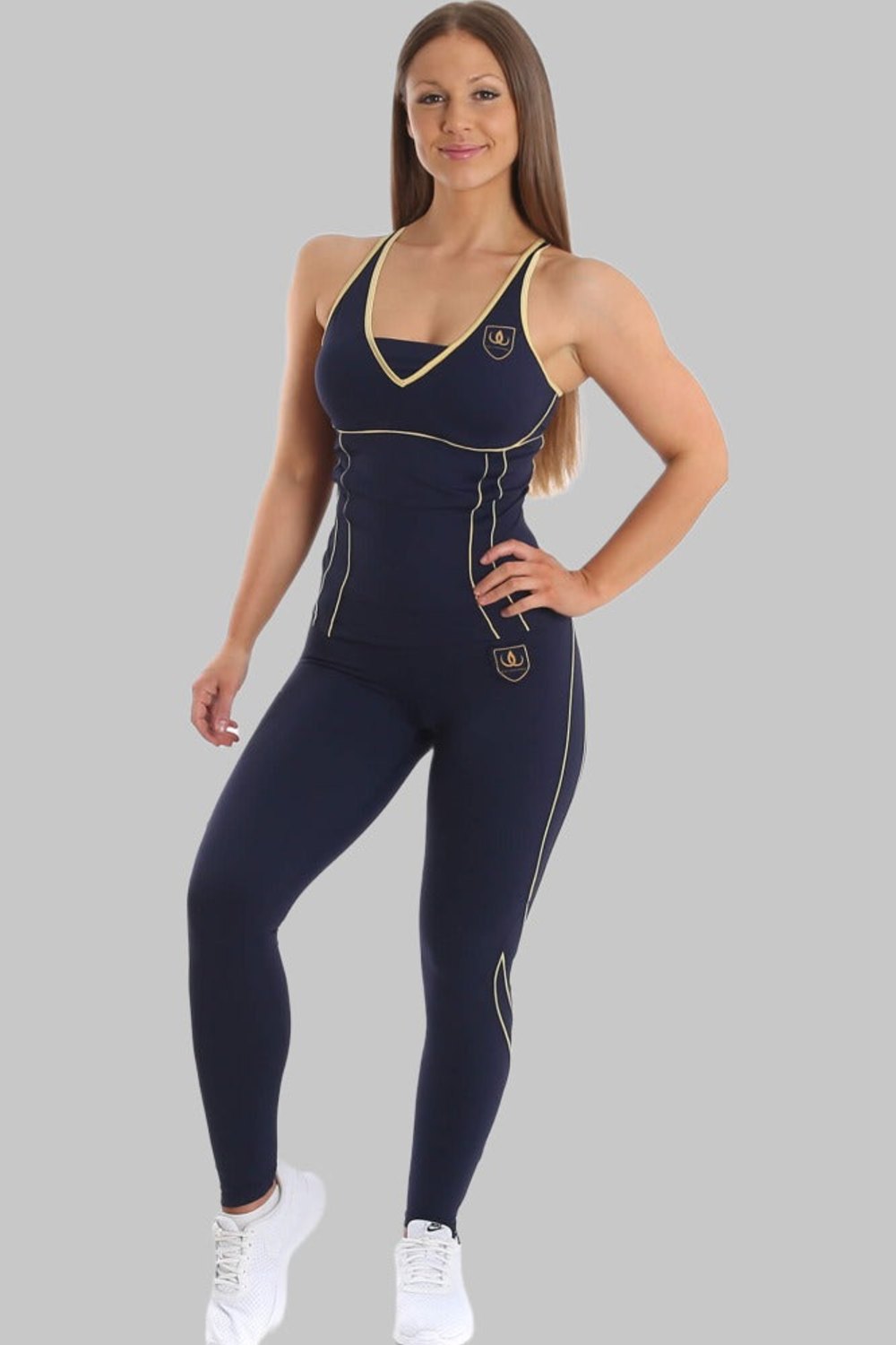 Le modèle se tient en débardeur bleu marine et legging bleu marine à lignes dorées, avec des baskets blanches.