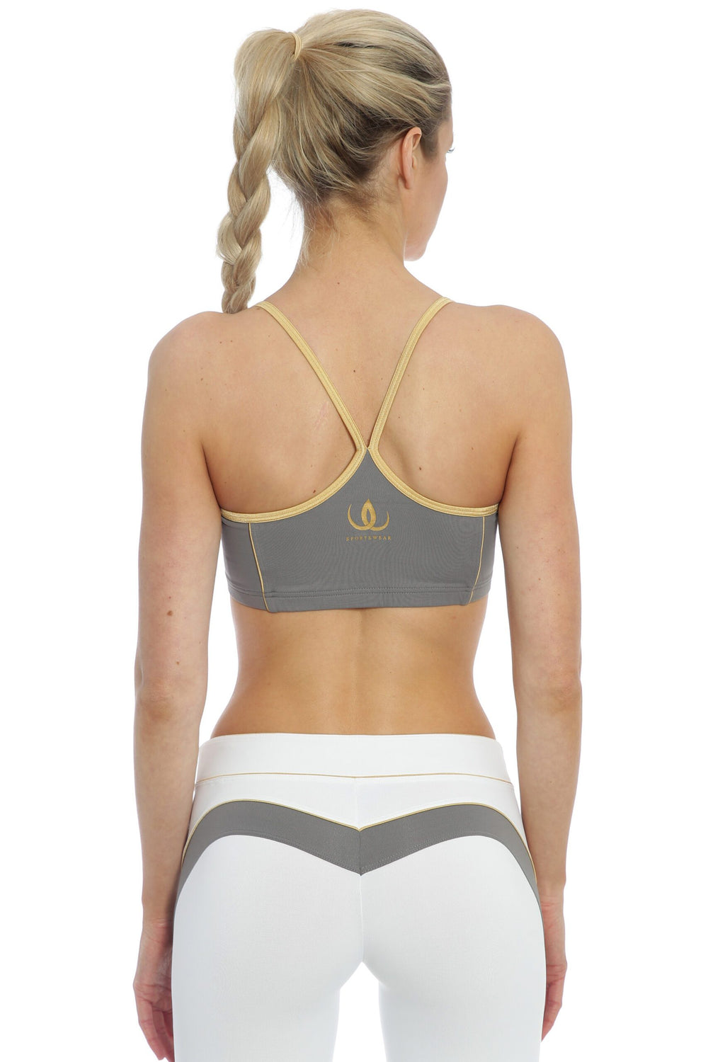 De fines bretelles bordées d'or se rejoignent en Y dans le dos du haut gris, porté avec un legging blanc.