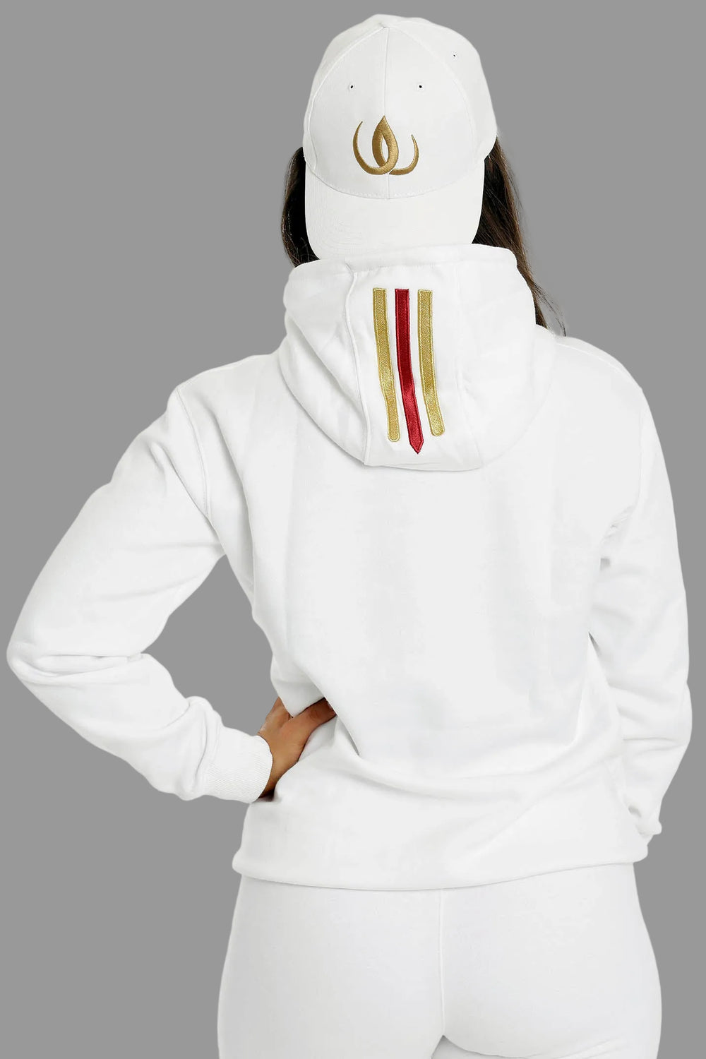 Dos du hoodie blanc avec deux rayures dorées et une rouge sur la capuche. Le mannequin porte une casquette blanche.