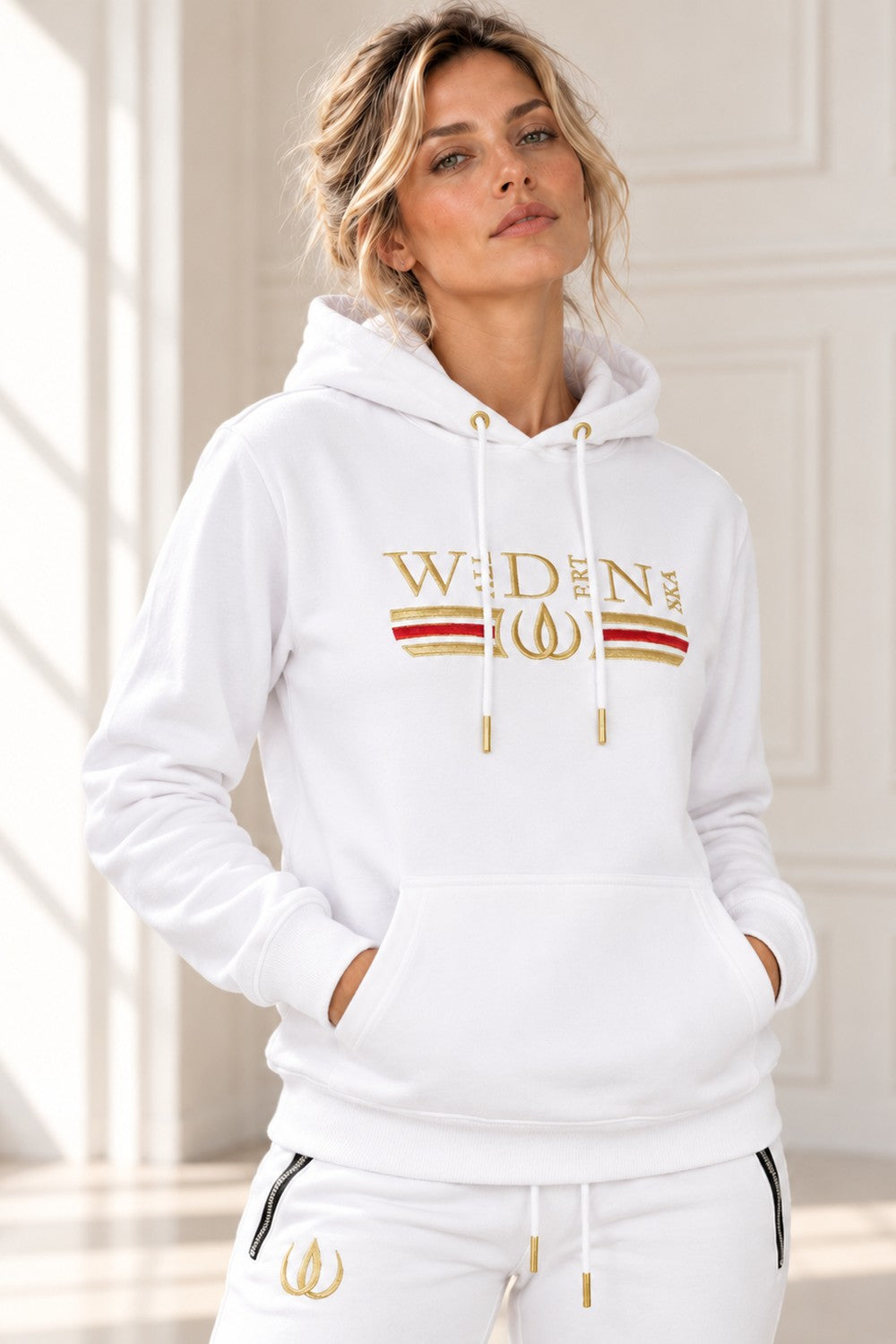 Deluxe Hoodie Blanc avec logo brodé doré, une bande rouge et dorée sur la poitrine et des cordons à embouts dorés.