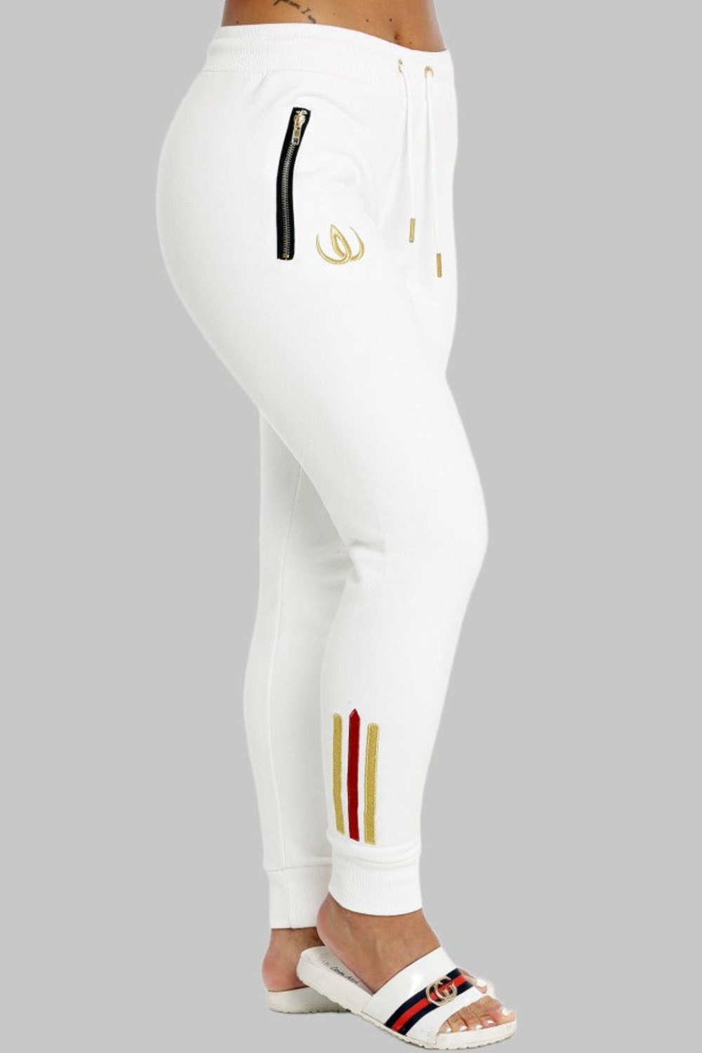 Jogging blanc de profil avec zip doré sur la poche, logo doré sur la cuisse et rayures à la cheville.