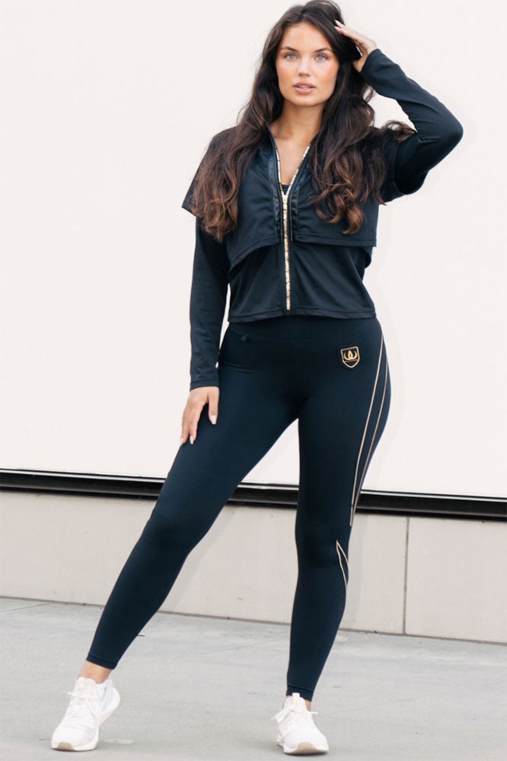 Le zip doré parcourt toute la veste, porté avec un legging noir à lignes dorées.