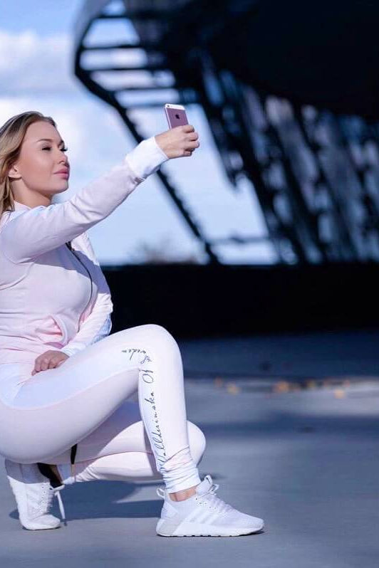 En extérieur sur un toit, le modèle est accroupi dans le pantalon de sport rose clair et la veste assortie.