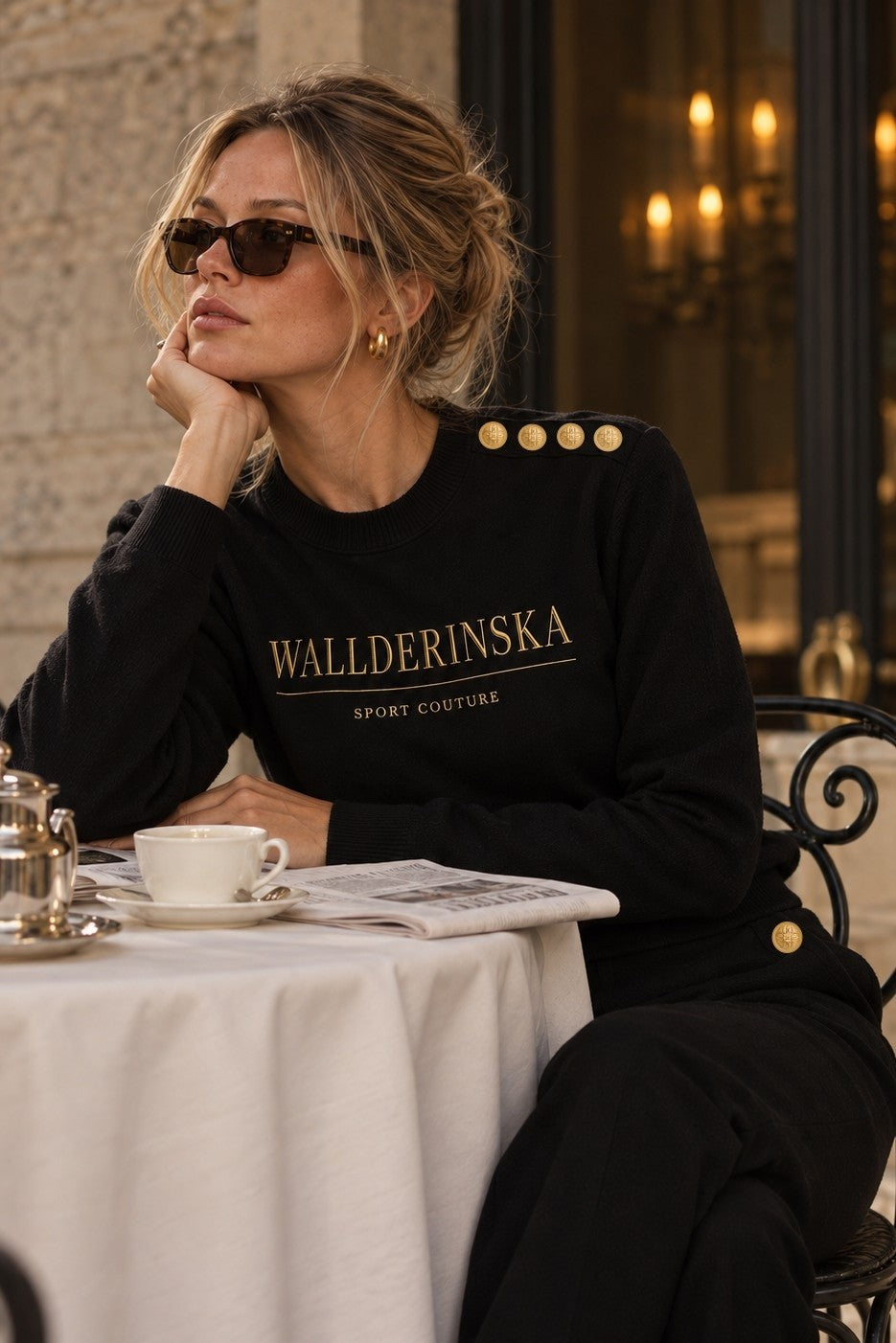 Pull Edge Gold Button en noir dans un café, avec les boutons dorés sur l'épaule.